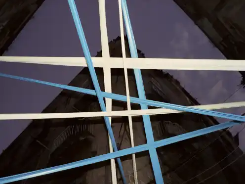Blue and white beams cross above a dark building facade.