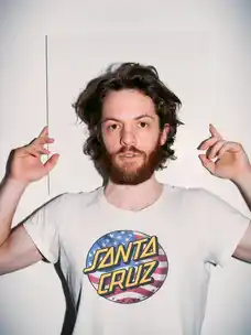 Portrait of Marlon Bienert in front of a white wall holding his hands up