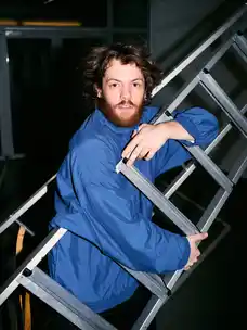 Portrait of Marlon Bienert with a blue jacket holding a ladder
