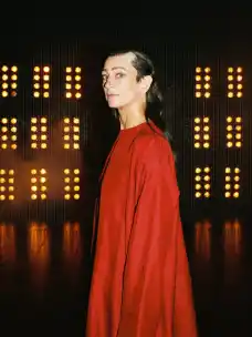 Wiebke Puls in a red costume backstage in front of illuminated stage curtains at The Master and Margarita